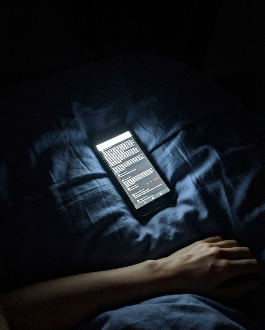 Un téléphone posé sur une couette dans une chambre sombre, son écran étant la seule lumière